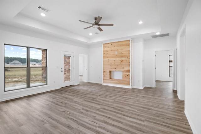 unfurnished living room featuring wood-type flooring, a raised ceiling, and ceiling fan