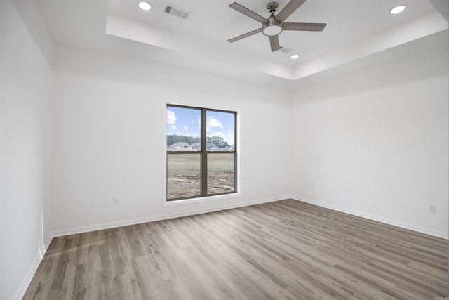 unfurnished room with ceiling fan, a tray ceiling, and light hardwood / wood-style floors