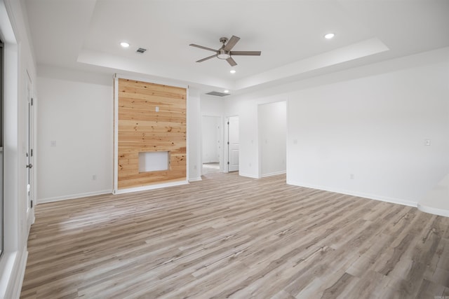 unfurnished living room with ceiling fan, a tray ceiling, and light hardwood / wood-style flooring