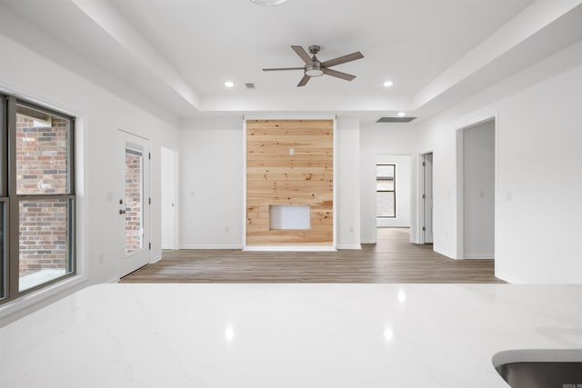 unfurnished living room with ceiling fan, hardwood / wood-style floors, plenty of natural light, and a tray ceiling