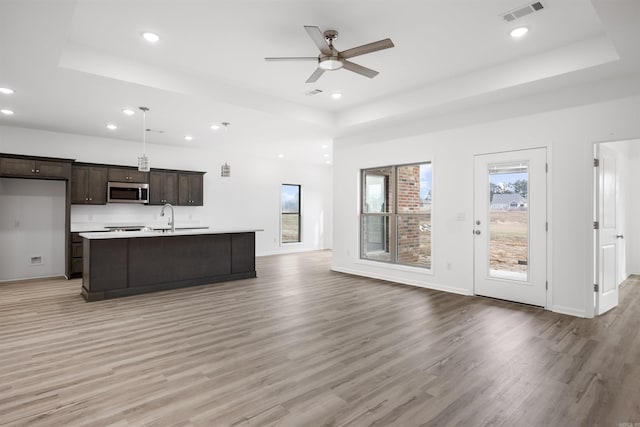 kitchen with a kitchen island with sink, a raised ceiling, ceiling fan, pendant lighting, and light hardwood / wood-style flooring