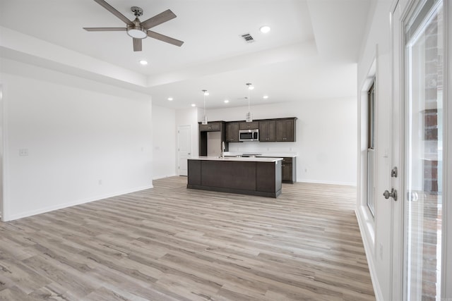 kitchen with light hardwood / wood-style floors, decorative light fixtures, a kitchen island with sink, and a tray ceiling