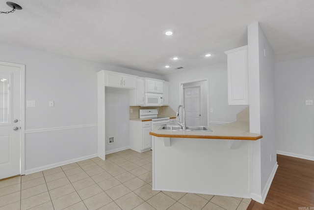 kitchen featuring white appliances, kitchen peninsula, white cabinetry, a kitchen breakfast bar, and sink