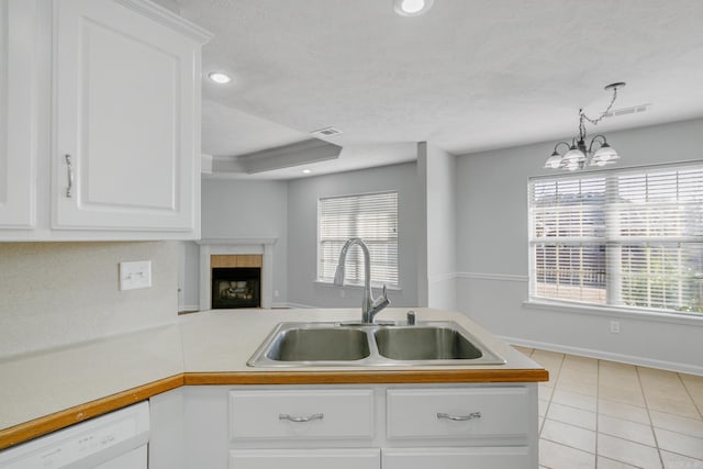 kitchen featuring white cabinets, dishwasher, a tiled fireplace, pendant lighting, and sink