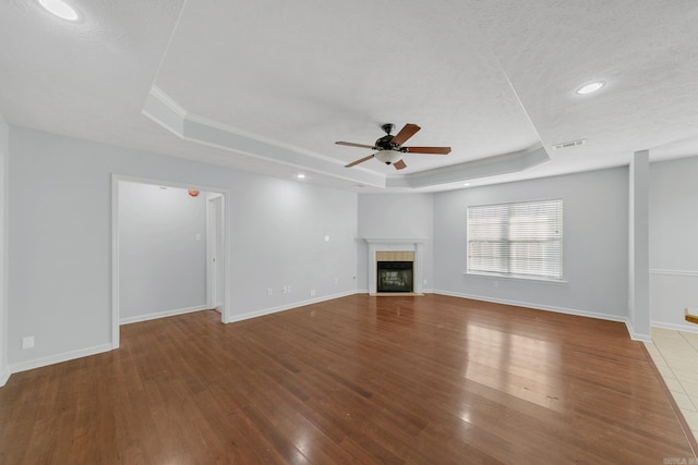 unfurnished living room with a fireplace, a raised ceiling, ceiling fan, and hardwood / wood-style flooring