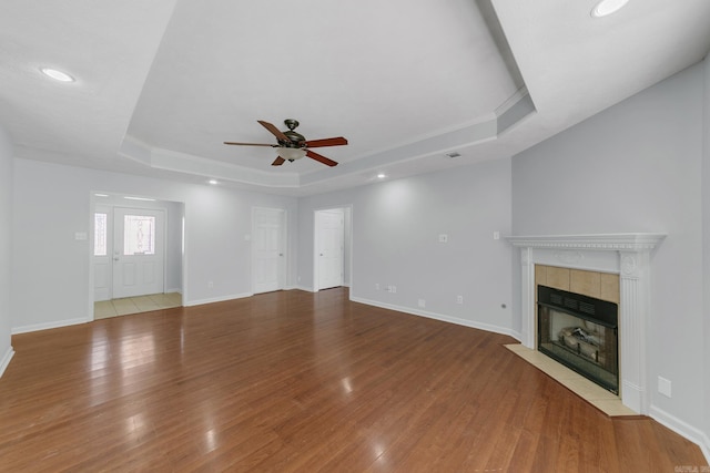 unfurnished living room with wood-type flooring, a raised ceiling, ceiling fan, and a tiled fireplace