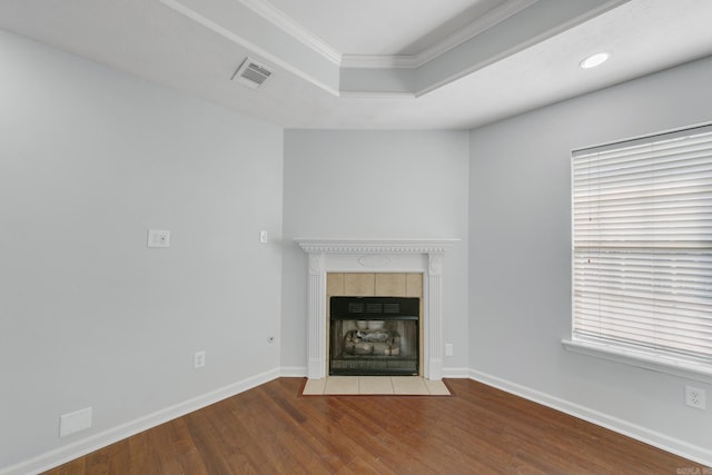 unfurnished living room with a tiled fireplace, a tray ceiling, ornamental molding, and wood-type flooring