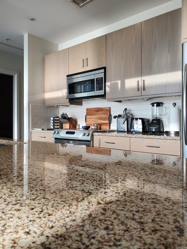 kitchen with light stone countertops, stainless steel appliances, and decorative backsplash