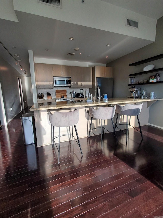 kitchen featuring sink, black built in fridge, light stone counters, a breakfast bar area, and dark wood-type flooring