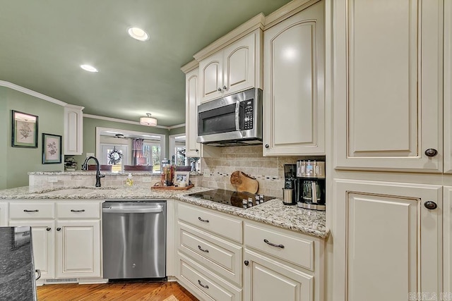 kitchen featuring stainless steel appliances, sink, cream cabinets, light stone counters, and light hardwood / wood-style flooring