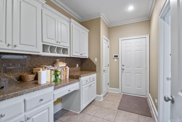 kitchen featuring built in desk, light tile patterned floors, ornamental molding, white cabinetry, and tasteful backsplash