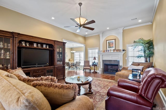 living room with a healthy amount of sunlight, hardwood / wood-style floors, crown molding, and ceiling fan with notable chandelier