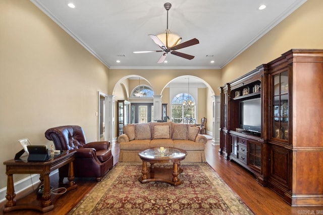 living room with ceiling fan with notable chandelier, decorative columns, ornamental molding, and dark wood-type flooring