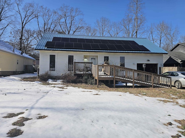 snow covered rear of property with solar panels, a garage, and a wooden deck