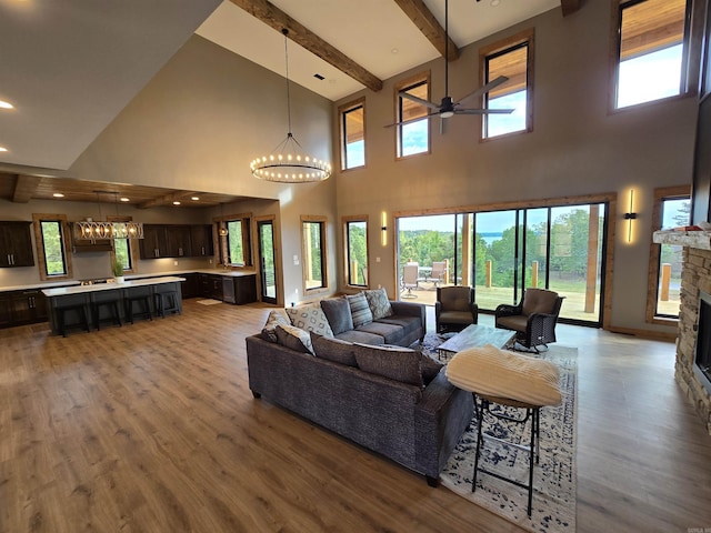 living room with a fireplace, beamed ceiling, hardwood / wood-style flooring, ceiling fan with notable chandelier, and a high ceiling