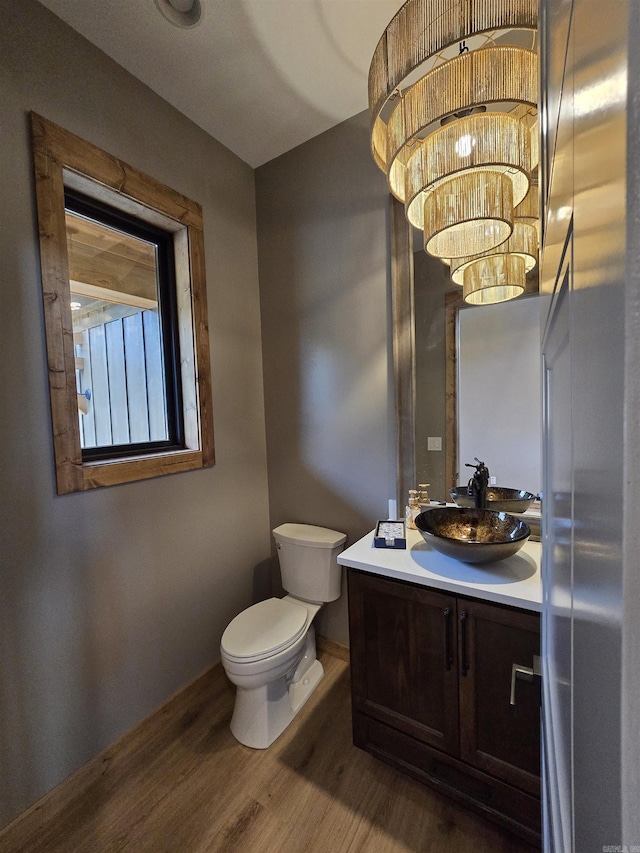 bathroom with wood-type flooring, a chandelier, vanity, and toilet