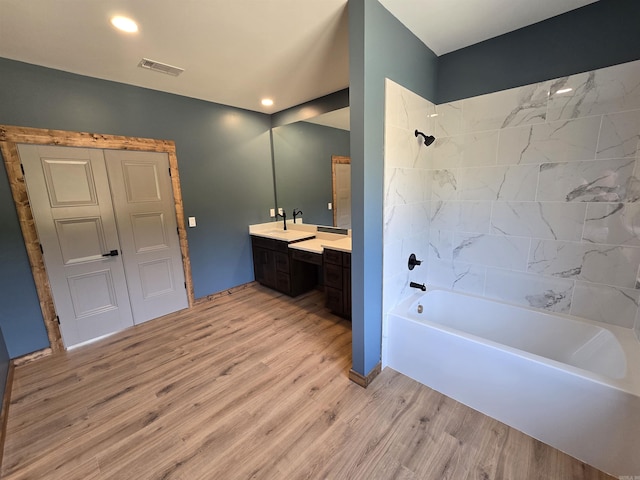 bathroom with hardwood / wood-style flooring, tiled shower / bath, and vanity