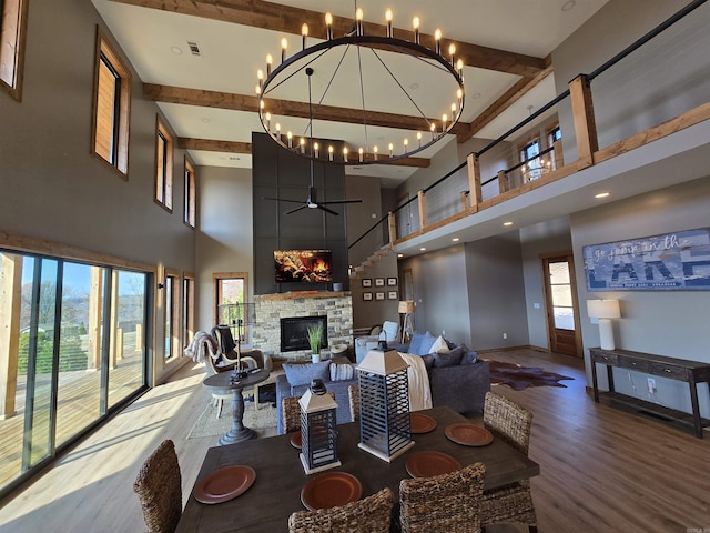 living room featuring ceiling fan with notable chandelier, hardwood / wood-style flooring, a towering ceiling, and a stone fireplace