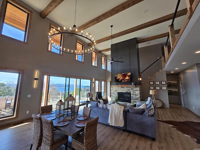 dining space featuring dark hardwood / wood-style floors, a high ceiling, beam ceiling, ceiling fan with notable chandelier, and a fireplace