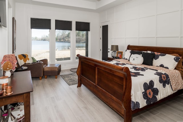 bedroom with multiple windows, light hardwood / wood-style flooring, and a water view