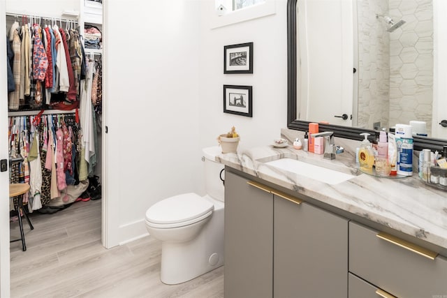 bathroom with toilet, tiled shower, wood-type flooring, and vanity