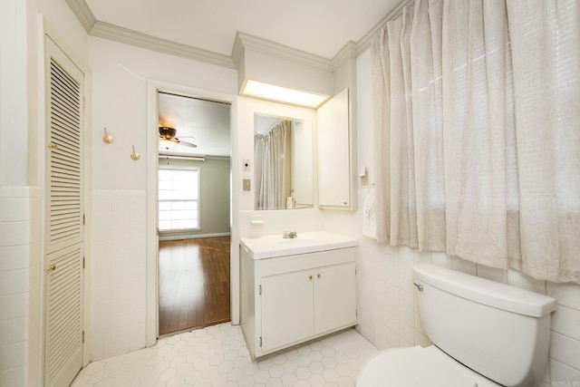 bathroom with tile patterned flooring, toilet, crown molding, vanity, and tile walls