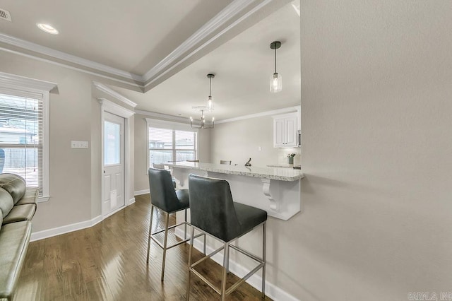 kitchen featuring a kitchen breakfast bar, hanging light fixtures, crown molding, light stone counters, and white cabinetry