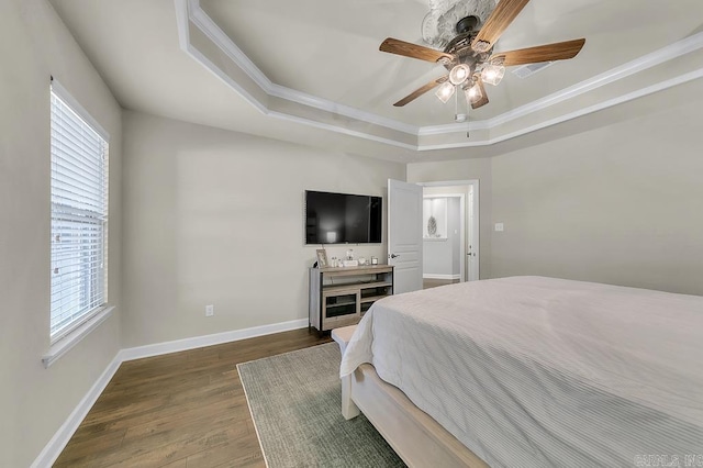 bedroom featuring ceiling fan, dark wood-type flooring, ornamental molding, multiple windows, and a tray ceiling