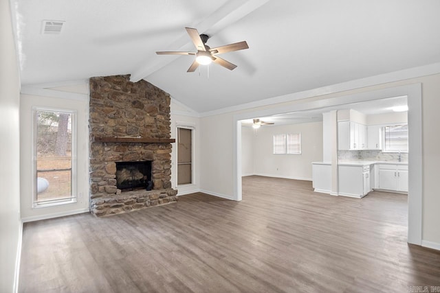 unfurnished living room featuring wood-type flooring, ceiling fan, vaulted ceiling with beams, and a stone fireplace