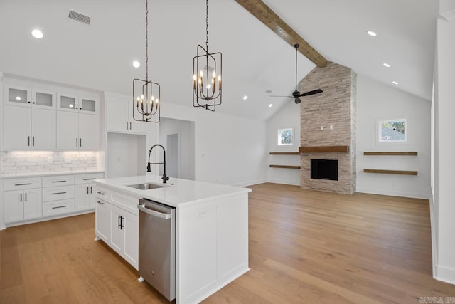 kitchen featuring sink, white cabinetry, stainless steel dishwasher, a center island with sink, and a stone fireplace