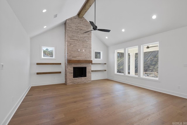 unfurnished living room featuring beamed ceiling, ceiling fan, hardwood / wood-style flooring, high vaulted ceiling, and a stone fireplace