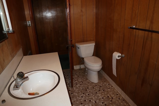 bathroom with toilet, tile patterned flooring, wood walls, and sink