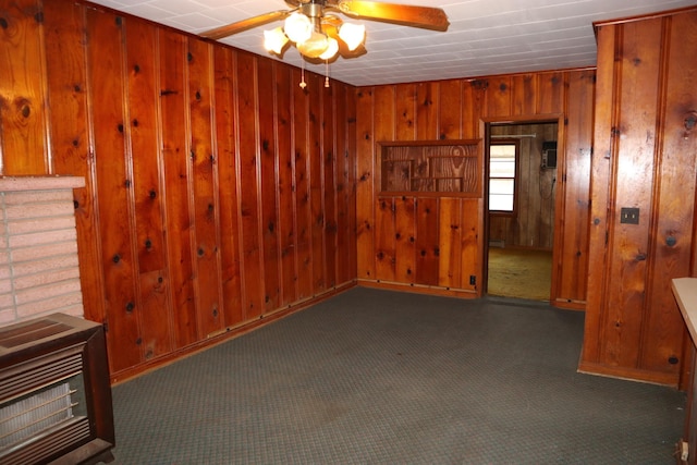 empty room with wooden walls, dark carpet, ceiling fan, and heating unit