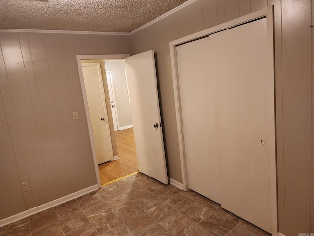 unfurnished bedroom with a textured ceiling, a closet, crown molding, and wooden walls