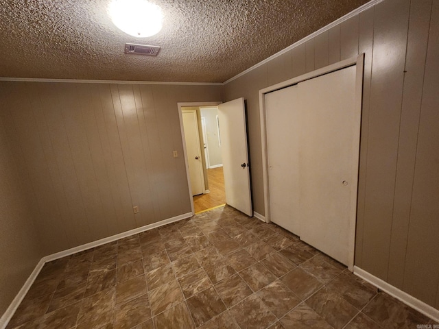 unfurnished bedroom with a closet, wooden walls, a textured ceiling, and ornamental molding