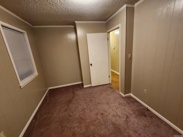 empty room with a textured ceiling, wooden walls, crown molding, and carpet flooring