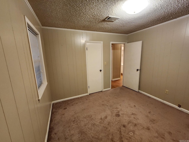 unfurnished bedroom featuring wooden walls, carpet flooring, a textured ceiling, and ornamental molding