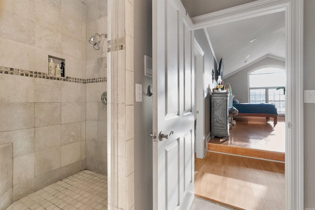 bathroom with a tile shower, wood-type flooring, vaulted ceiling, and crown molding