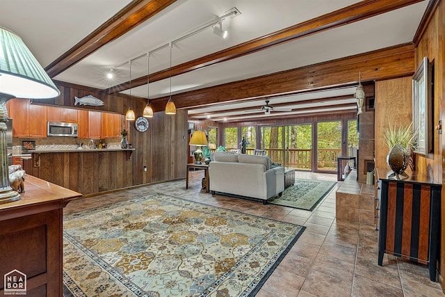 living room featuring rail lighting, wood walls, and beamed ceiling