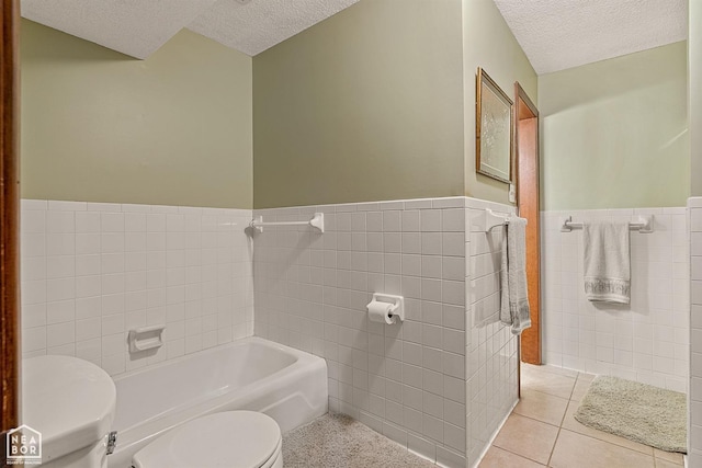 bathroom with a textured ceiling, tile patterned floors, tile walls, toilet, and a washtub