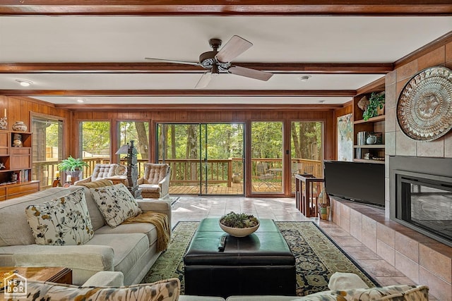 living room with beamed ceiling, a fireplace, wooden walls, light tile patterned flooring, and ceiling fan