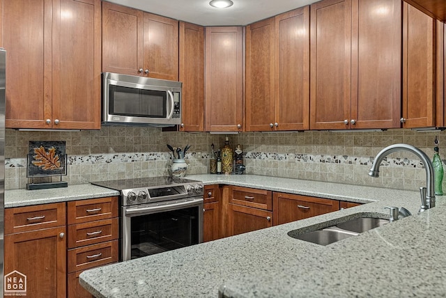 kitchen featuring light stone countertops, backsplash, appliances with stainless steel finishes, and sink