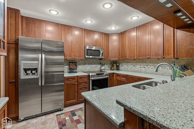 kitchen featuring kitchen peninsula, stainless steel appliances, backsplash, light stone countertops, and sink