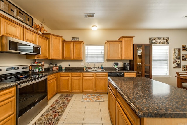 kitchen featuring stainless steel appliances, light tile patterned floors, a kitchen island, dark stone countertops, and sink