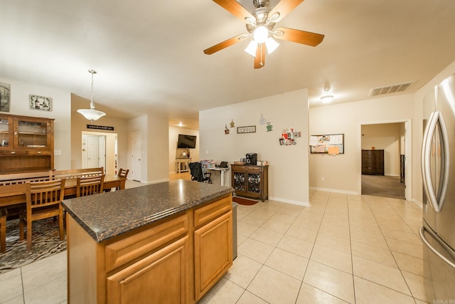 kitchen featuring hanging light fixtures, light tile patterned floors, ceiling fan, stainless steel fridge, and a kitchen island