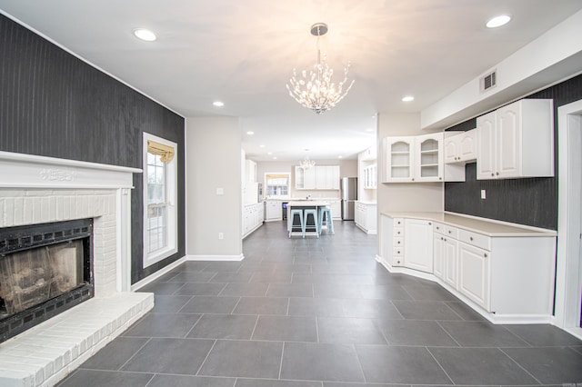 kitchen featuring a chandelier, hanging light fixtures, stainless steel fridge, a fireplace, and white cabinetry