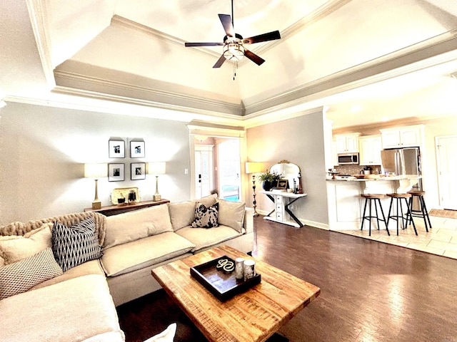 living room with ceiling fan, dark wood-type flooring, a raised ceiling, and crown molding