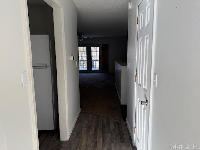 hall with french doors, a textured ceiling, and dark wood-type flooring