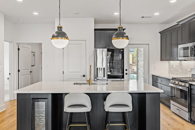 kitchen featuring wine cooler, a kitchen island with sink, pendant lighting, and appliances with stainless steel finishes