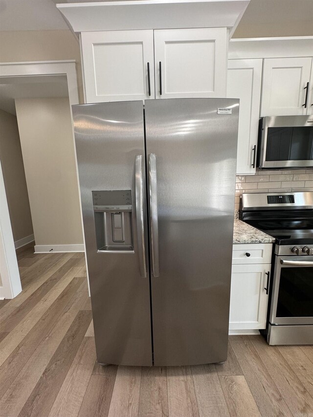 kitchen with white cabinets, light stone counters, light hardwood / wood-style flooring, backsplash, and appliances with stainless steel finishes